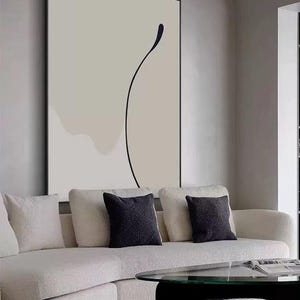 Puede incluir: Un sof&aacute; seccional blanco con tres cojines negros frente a una gran pintura abstracta con una l&iacute;nea negra sobre fondo blanco.