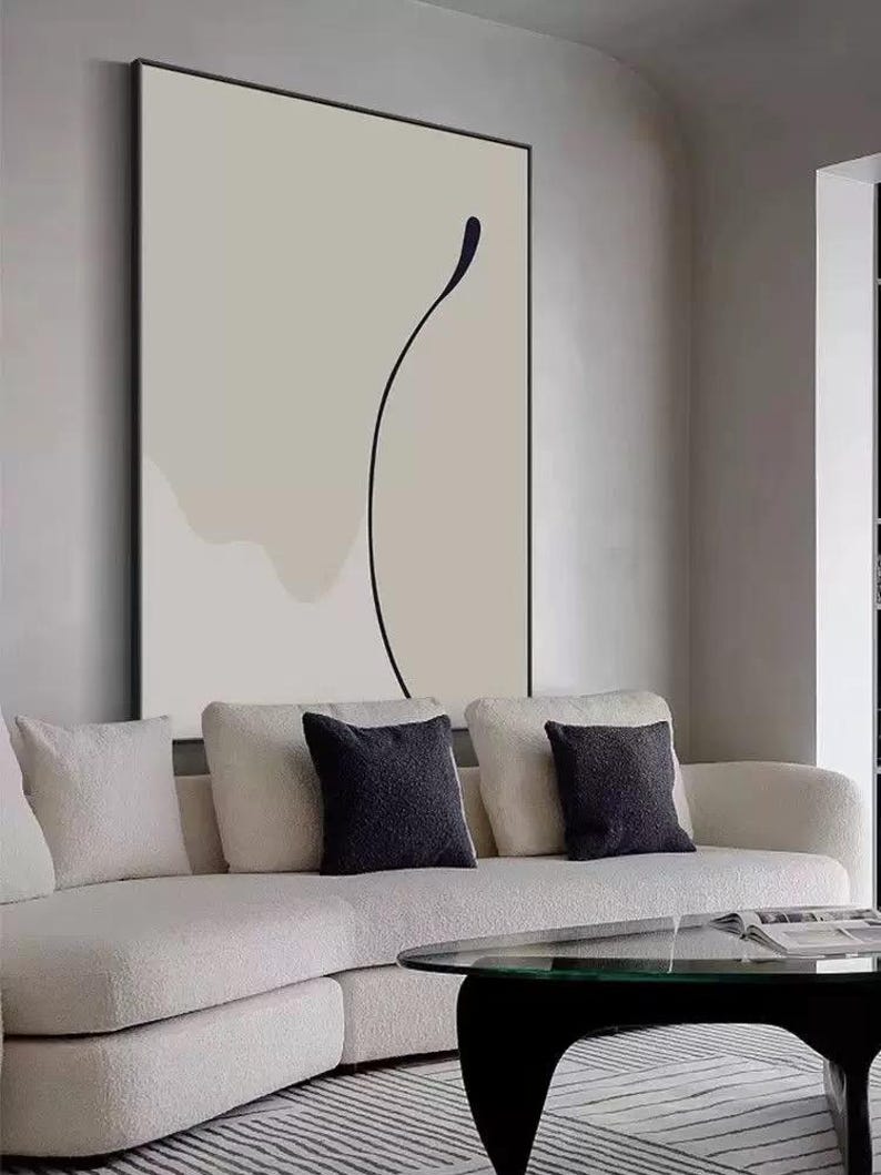 Puede incluir: Un sof&aacute; seccional blanco con tres cojines negros frente a una gran pintura abstracta con una l&iacute;nea negra sobre fondo blanco.