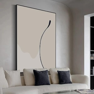Puede incluir: Impresi&oacute;n de arte abstracto con un fondo beige y un dibujo de l&iacute;nea negra de una forma curva. La impresi&oacute;n est&aacute; enmarcada y colgada en una pared sobre un sof&aacute; blanco.