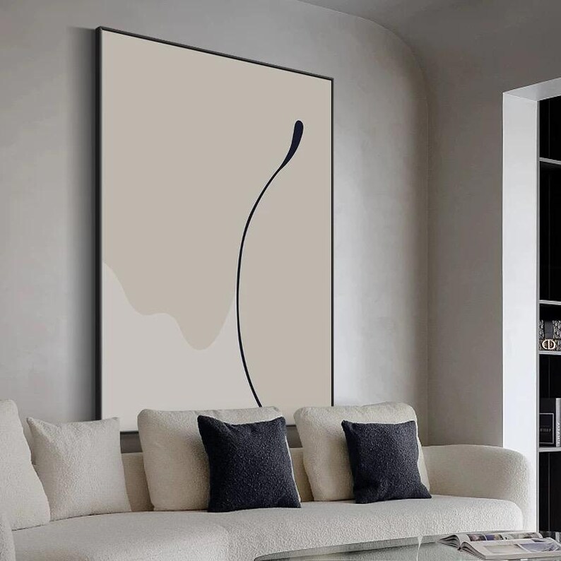 Puede incluir: Impresi&oacute;n de arte abstracto con un fondo beige y un dibujo de l&iacute;nea negra de una forma curva. La impresi&oacute;n est&aacute; enmarcada y colgada en una pared sobre un sof&aacute; blanco.