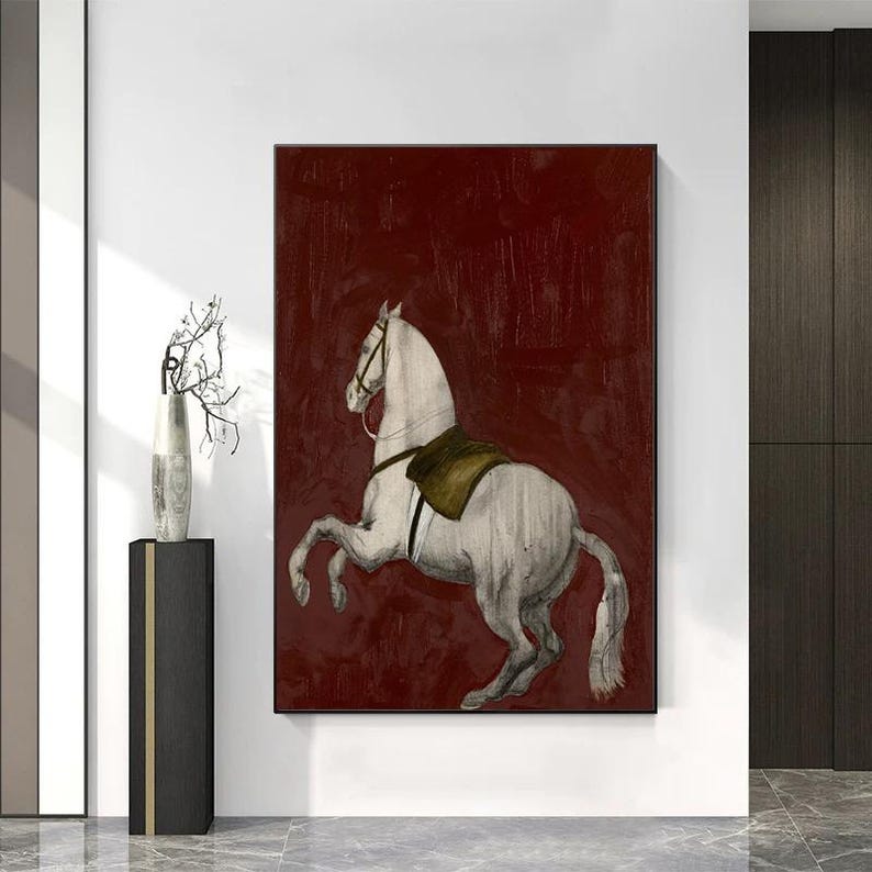 May include: A framed canvas print featuring a white horse rearing up against a deep red background. The horse has a saddle and bridle. The artwork is displayed on a white wall.