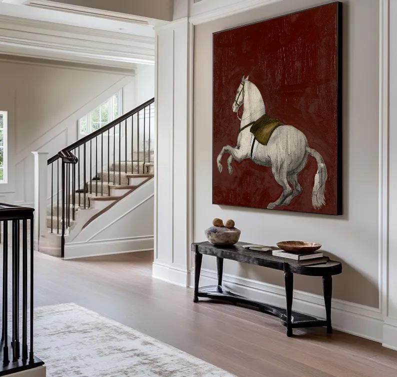 May include: A large framed canvas art piece featuring a white horse rearing up against a deep red background. The horse has a saddle and bridle. The artwork hangs above a black bench with decorative items.