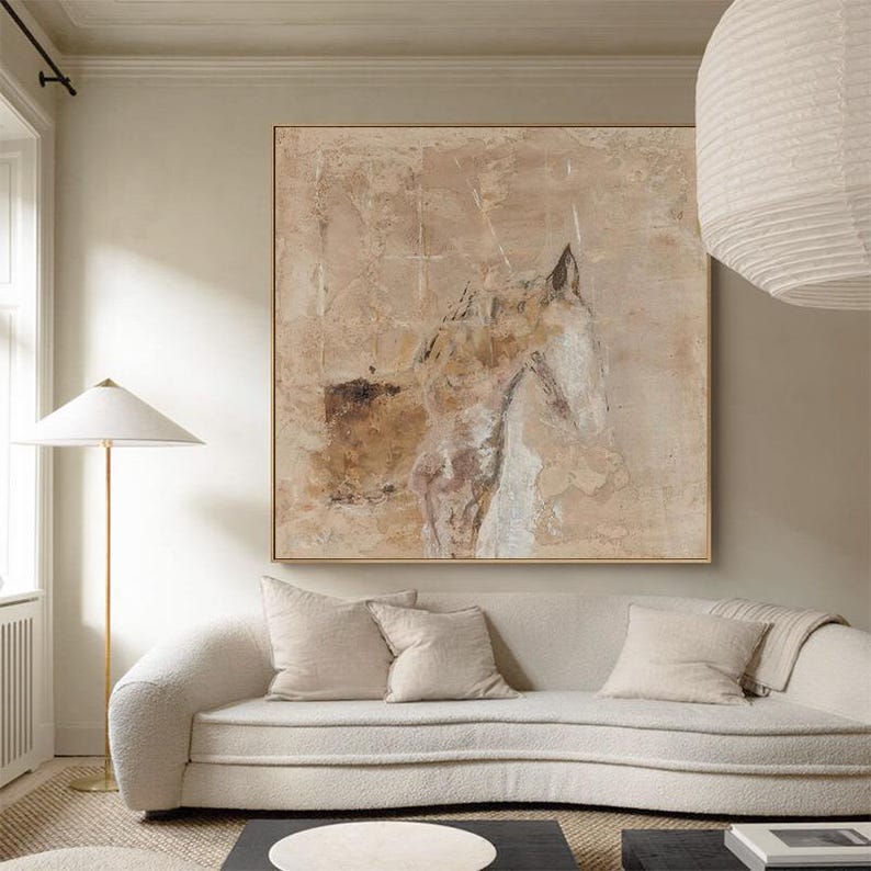 May include: Abstract painting of a horse's head in shades of brown, beige, and white. The painting is displayed on a wall above a white sofa with pillows.