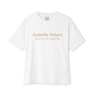 May include: A white t-shirt featuring the text "Isabella Solarz" and "@reclaiming_happiness" in brown. The shirt has a crew neck and short sleeves. A small design is visible near the collar.