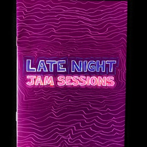 May include: A purple notebook featuring a wavy line design. The text "LATE NIGHT JAM SESSIONS" is written in a neon-style font. The notebook is set against a black backdrop.