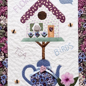 Könnte beinhalten: Eine gesteppte Wanddekoration mit einem Vogelhaus, einer Teekanne und Blumen. Das Vogelhaus hat ein lila Dach und eine Katzenfigur. Unten befindet sich eine blaue Teekanne mit floralen Mustern. Die Worte "FLOWERS", "TEA" und "BIRDS" sind gestickt.