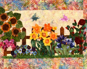 May include: A colourful quilted wall hanging depicting a garden scene with a brown picket fence, sunflowers, daffodils, purple flowers, and red roses. Butterflies are flying above the fence.