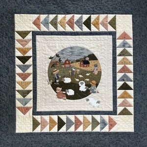 May include: A quilted wall hanging depicting a farmhouse scene with a red barn, a field of sheep, and children. The quilt is bordered with a patchwork of triangles in shades of brown, blue, and pink.