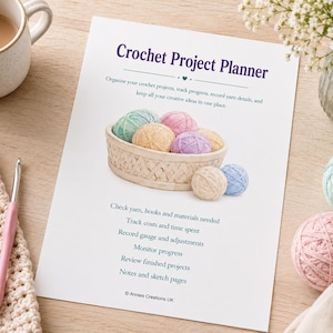 Może przedstawiać: Biała kartka papieru z tytułem Crochet Project Planner oraz koszykiem kolorowych kłębków włóczki. Tekst wymienia funkcje do śledzenia projektów, kosztów i materiałów. Zawiera sekcje na notatki i szkice od Annies Creations UK.