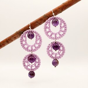 May include: A pair of dangle earrings with two crocheted circles and amethyst beads. The earrings are a light purple color.