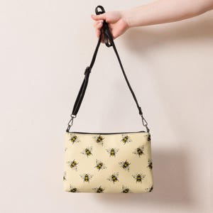May include: A yellow crossbody bag with a black strap and a pattern of bees.