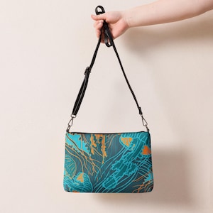 May include: A rectangular crossbody bag with a black strap, featuring a teal and orange jellyfish pattern. The bag has a black zipper and a black strap. The jellyfish design is a repeating pattern across the bag's surface.