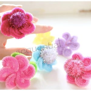 Pu&ograve; includere: Un set di sei anelli di fiori colorati in filo di ferro. Gli anelli sono fatti di filo di ferro e hanno una variet&agrave; di colori, tra cui rosa, blu, viola e giallo. Gli anelli sono decorati con glitter e pompon.