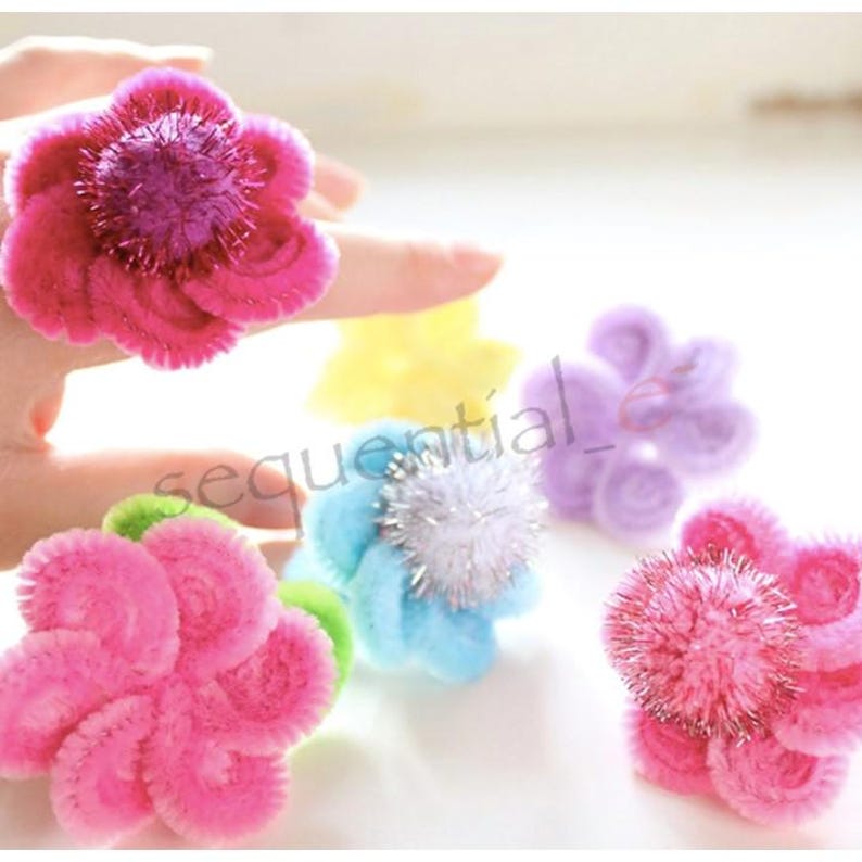 Pu&ograve; includere: Un set di sei anelli di fiori colorati in filo di ferro. Gli anelli sono fatti di filo di ferro e hanno una variet&agrave; di colori, tra cui rosa, blu, viola e giallo. Gli anelli sono decorati con glitter e pompon.