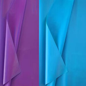 Può includere: Una vista a schermo diviso mostra due fogli di materiale liscio e semitraslucido. Il lato sinistro presenta un foglio viola vibrante con una lucentezza morbida, mentre il lato destro mostra un foglio blu ciano brillante con una finitura liscia.