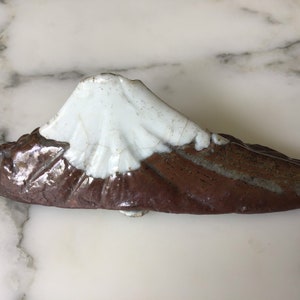 May include: A ceramic sculpture of Mount Fuji, a Japanese mountain, with a white top and a brown base.