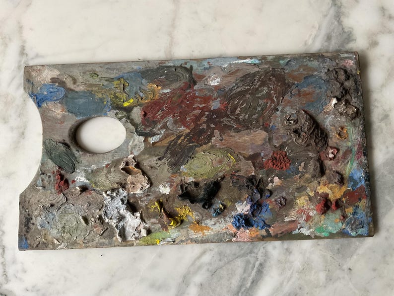 K&ouml;nnte beinhalten: Eine gebrauchte Holzmalpalette, bedeckt mit getrockneter Farbe. Die Palette hat ein Daumenloch und ist stark mit verschiedenen Farben wie Rot, Blau, Gelb und Braun befleckt. Die Palette ist rechteckig mit einer gebogenen Kante.