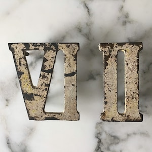 May include: Two metal Roman numeral house numbers, VI and II, are displayed on a white marble background. The numbers are painted in a distressed gold finish.