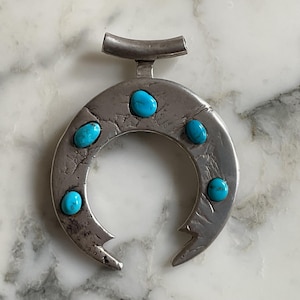May include: A silver pendant in the shape of a crescent moon with six turquoise stones set into the metal.