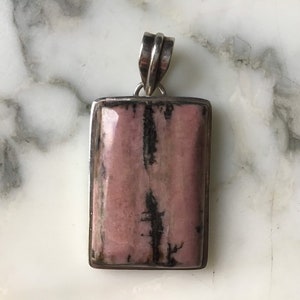 May include: A silver pendant with a rectangular pink and black stone.