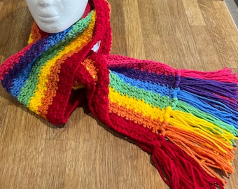 May include: A handmade rainbow scarf with red fringe. The scarf is crocheted with stripes of red, orange, yellow, green, blue, and purple. The scarf is draped over a white mannequin head.