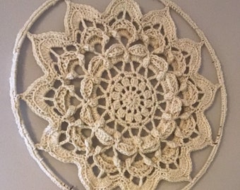 May include: A large, cream-colored crocheted mandala hanging on a wall. The mandala is made of a delicate, intricate pattern of stitches.