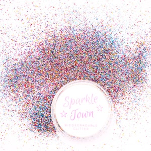 May include: A close-up of a clear plastic container filled with multi-colored glitter. The container has a white label with the text "Sparkle Town" and "Biodegradable Glitter".