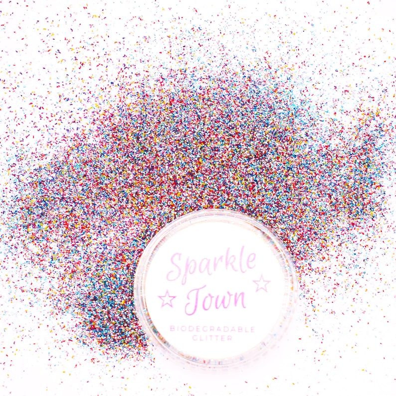 May include: A close-up of a clear plastic container filled with multi-colored glitter. The container has a white label with the text "Sparkle Town" and "Biodegradable Glitter".