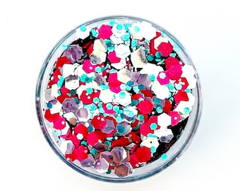 May include: A clear plastic container filled with a mix of glitter. The glitter includes various shapes and sizes in shades of red, silver, white, and teal. The container is round and sits against a white background.