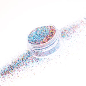 May include: A clear jar filled with colorful glitter, with some glitter spilling out onto a white surface.