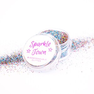 May include: A clear plastic jar filled with multi-colored glitter. The jar has a white label with the text "Sparkle Town" in pink lettering and the words "Biodegradable Glitter" in black lettering.