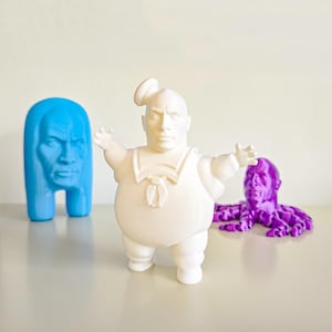 Può includere: Tre figurine stampate in 3D: un fantasma bianco con colletto da marinaio, una figura umanoide blu e un polpo viola.