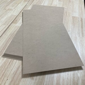 May include: A stack of brown cardboard sheets on a light wood surface.