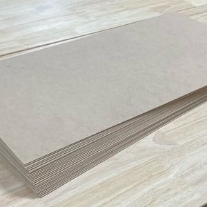May include: A stack of brown cardboard sheets on a light wood surface.