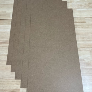 May include: A stack of six brown cardboard sheets. The sheets are rectangular and have a rough texture.