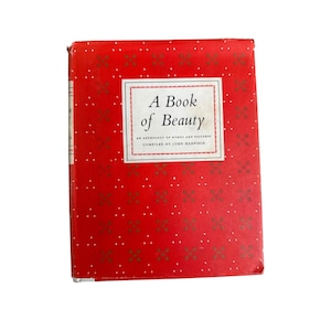 May include: A vintage book titled "A Book of Beauty" with a red cover adorned with white polka dots and floral patterns. The title is in a white frame. The book is an anthology of words and pictures, compiled by John Hadfield.