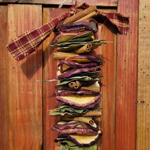 May include: A dried fruit and spice garland with cinnamon sticks, dried apple slices, and bay leaves tied together with a red and white plaid ribbon.