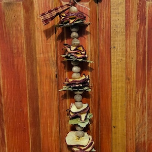 May include: A rustic fall garland with dried apple slices and bay leaves strung on wooden beads. The garland is tied with a red and brown plaid ribbon.