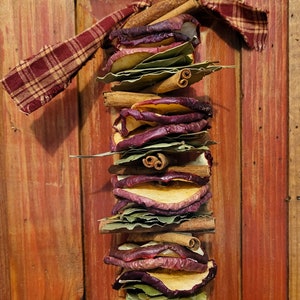May include: A rustic, homemade, fall-themed garland with dried apple slices, cinnamon sticks, and bay leaves tied together with a plaid fabric ribbon.