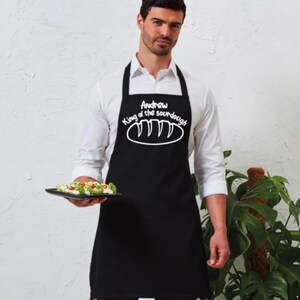May include: Black apron with white text that reads "Andrew King of the sourdough" with a drawing of a loaf of bread.