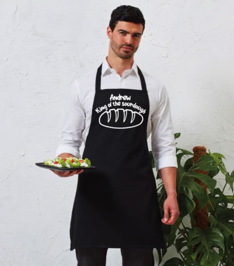 May include: Black apron with white text that reads "Andrew King of the sourdough" with a drawing of a loaf of bread.