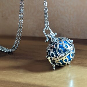 May include: A silver chain necklace with a blue and silver cage-like pendant. The pendant has a delicate design and is shaped like a sphere.