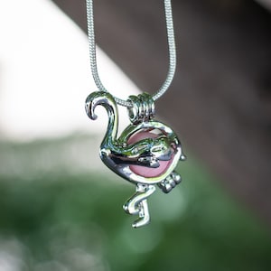 May include: A silver flamingo charm necklace with a pink glass orb inside. The necklace is on a silver chain.