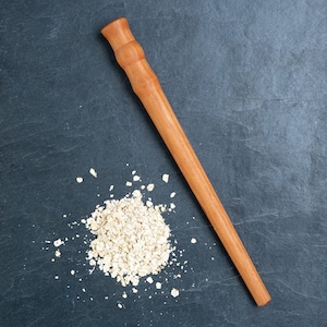 Peut inclure: Un rouleau à pâtisserie en bois sur une surface gris foncé avec un tas de flocons d'avoine.