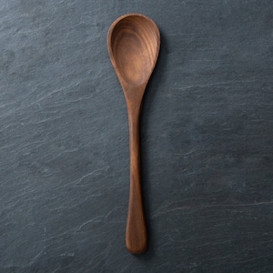 May include: A wooden spoon with a long handle and a rounded bowl. The spoon is made of a dark brown wood and is set against a dark gray background. The spoon is approximately 12 inches long.