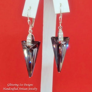 May include: A pair of silver dangle earrings featuring a dark purple crystal teardrop shape. The crystal is faceted and has a silver setting with small clear crystals.