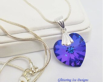 May include: A silver chain necklace with a heart-shaped pendant. The pendant is made of a clear crystal with a blue and purple iridescent finish. The pendant is about 1 inch in diameter. The necklace is 18 inches long.