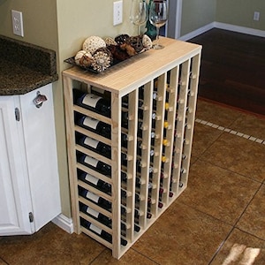 May include: A wooden wine rack with 12 rows of slots for storing wine bottles. The rack is made of natural wood and has a light brown finish. The rack is standing on a tiled floor.