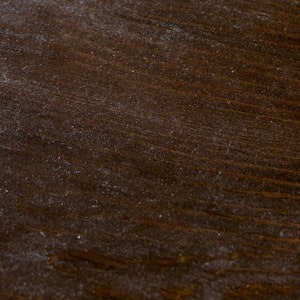 May include: A close-up of a dark brown wooden surface with a grainy texture. The surface is covered in a fine layer of dust.