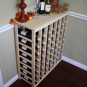 May include: A wooden wine rack with 72 bottle slots. The rack is made of natural wood and has a light brown finish. The rack is standing on a wooden floor.